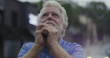 Yüzüne yapışmış elleri tutan yaşlı bir adam, yağmurda parlayan gözler, duygu, umut, ya da ruhsal bağlantı anında sessiz dua ile dolu.