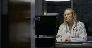 Kadın doktor gece geç saatlere kadar tıp ofisinde çalışıyor, klavyeye yazıyor, odaklanmış ve konsantre olmuş, profesyonel sağlık hizmetleri ortamı