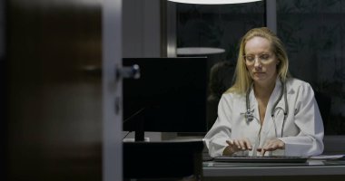 Kadın doktor gece geç saatlere kadar tıp ofisinde çalışıyor, klavyeye yazıyor, odaklanmış ve konsantre olmuş, profesyonel sağlık hizmetleri ortamı