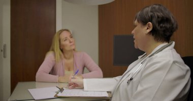 Klinikteki masadaki düşünceli tartışmalar sırasında doktorlara sağlık sorunlarını açıklayan orta yaşlı bir hasta.