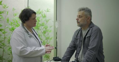 Klinikte tıbbi danışmanlık sırasında zor durumda olan orta yaşlı erkek hastaya destek veren kadın doktor