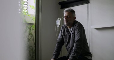 Muayene masasında sessizce otururken erkeklerin ellerinin üzerinde durması duygusal yorgunluk ya da yansıma belirtileri gösteriyor.