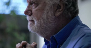 Umudun ve yansımanın yumuşak ifadesiyle yukarı bakan yaşlı bir adam, yan profili çerçevelenmiş, kapalı arka planda nazik