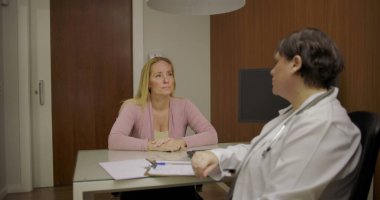 Klinikteki masadaki düşünceli tartışmalar sırasında doktorlara sağlık sorunlarını açıklayan orta yaşlı bir hasta.