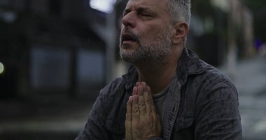 Orta yaşlı, gözleri kapalı ve elleri umutsuzca dua eden ya da duygusal yalvaran, rai 'de duran bir adam.