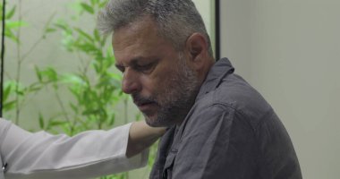 Muayene sırasında zor teşhislere tepki veren orta yaşlı erkek hastaların yakın çekimleri, klinik ortamlarda doktor tarafından desteklenirken duygusal tepkiler