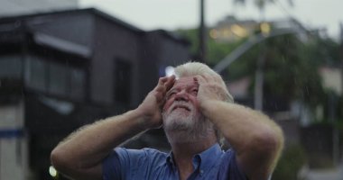 Yağmurun altında başıyla acı çeken yaşlı bir adam, gözleri kapalı, duygusal acı ve umutsuzlukla boğulmuş bir ifade.