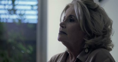 Yaşlı kadın yukari yukari yukari bakiyor, nazikçe dusunuyor, yumusak isik pencerenin yaninda duruyor, gozler duygu ve sessiz güçle dolu.