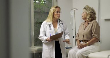 Kadın doktor, klinikte muayene sırasında klinikteki yaşlı kadın hastaya tıbbi bilgileri açıklıyordu.