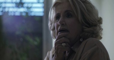 Yakın profil içinde orta yaşlı bir kadın, sakin, yansıtıcı bir ifadeyle, yumuşak arka plan ışığıyla çerçevelenmiş bir şekilde ileriye bakıyor.