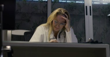 Yorgun kadın doktor, masa başında oturuyor. Uzun bir vardiyadan sonra bunalmış ve stresli. İş yerinde bitkinlik ve yorgunluğun duygusal ifadesi.