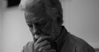 Siyah beyaz giymiş yaşlı bir adam duygusal bir yansıma içinde, yalnızlık anında aşağıya bakıyor.