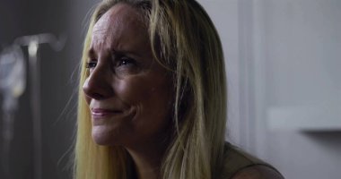 Klinik ortamda gözyaşlarını tutan kadının yakın plan çekimi, keder ve acıyla dolu ifade, yüzünde ve postomda hafif gerilim