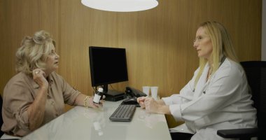 Klinikte kadın doktorla konuşurken elinde ilaç şişesi tutan yaşlı bir hasta.