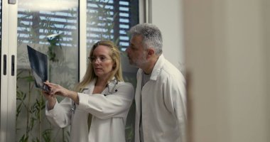 Kadın ve erkek doktorlar birlikte röntgen analizi yapıyor ve klinik ortamdaki tıbbi teşhisi tartışıyorlar.