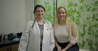 Gülümseyen doktor ve orta yaşlı kadın hasta yeşil bambu geçmişi olan klinikteki başarılı sağlık muayenesinden sonra poz veriyorlar.
