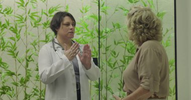 Kadın doktor aktif nişancılarla klinik ziyareti sırasında muayene masasında kıdemli hastaya sağlık sorununu açıklıyor