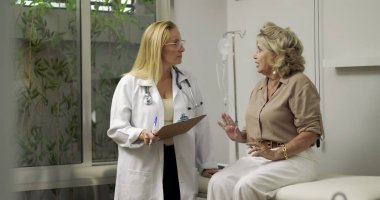 Kadın doktor, klinikte muayene sırasında klinikteki yaşlı kadın hastaya tıbbi bilgileri açıklıyordu.