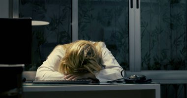 Kadın doktor gece geç saatlere kadar çalışırken masaya yaslanıyor. Yorgun ve bitkin görünüyor.