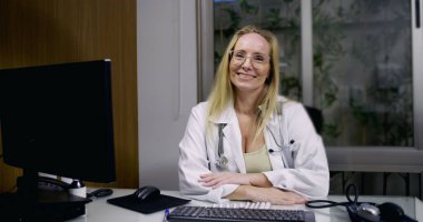 Modern klinikteki masasında güvenle gülümseyen kadın doktor hasta danışmanlığına ve profesyonel tıbbi tedaviye hazır.