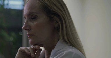 Yan profildeki kadın doktor, elleri çenesinin altında, gözleri klinik ortamda derin bir yansıma anında ileri bakıyor.