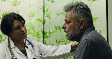 Kadın doktor, klinikte duygusal konuşmalar sırasında orta yaşlı bir erkek hastayla nazikçe konuşuyor ve omuz omuza destek veriyor.