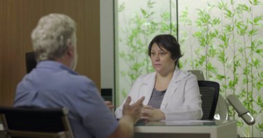 Klinikteki muayene sırasında doktora semptomları açıklayan hasta, el hareketleriyle ve sağlık hizmetleriyle ilgili konuşmalarla meşgul.