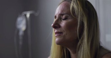 Klinik ortamda gözyaşlarını tutan kadının yakın plan çekimi, keder ve acıyla dolu ifade, yüzünde ve postomda hafif gerilim