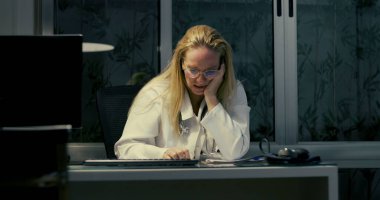 Kadın doktor gece geç saatlere kadar çalışırken masaya yaslanıyor. Yorgun ve bitkin görünüyor.