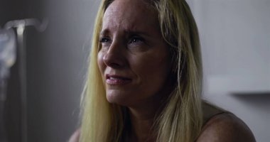 Klinik ortamda gözyaşlarını tutan kadının yakın plan çekimi, keder ve acıyla dolu ifade, yüzünde ve postomda hafif gerilim