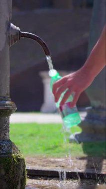 Şehir parkındaki halka açık çeşmeden gelen temiz suyla doldurulmuş plastik şişe, susuzluk, ferahlık ve açık havada sürdürülebilir yeniden kullanımın sembolü.