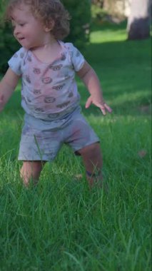 Kıvırcık saçlı çocuk yeşil çimenlerde yürümeyi öğrenirken tökezliyor, düşüyor ve çocukluk yıllarının masumiyeti ve kararlılığıyla ayağa kalkıyor.