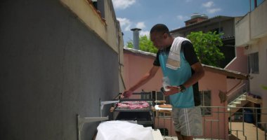 Bir siyah adam açık havada et tatlandırıyor, Latin Amerika 'nın arka bahçesinde konut binalarıyla barbekü hazırlıyor.