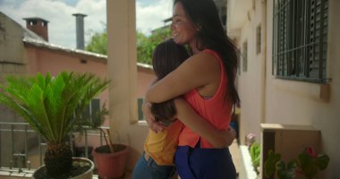 Anne, Güney Amerika 'da bir mahallede küçük kızına sıcak bir şekilde sarılıp şefkatli ve sevgi dolu bir aile bağını paylaşıyor.