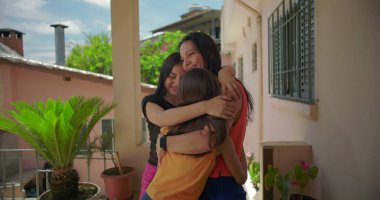 Anne iki kızı kucaklıyor, hepsi de sıcak bir şekilde kucaklıyor ve sevgisini ve bağlantısını ifade ediyor, Latin Amerika 'nın yeşillikli yerleşim bölgesinde.