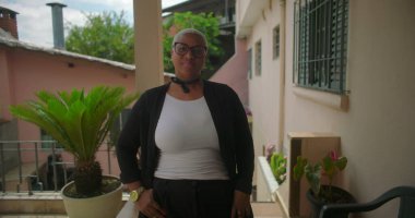 Latin Amerika 'nın bir mahallesinde terasta güven içinde duran, rahat bir ortamda gururunu ve zarafetini sergileyen Afrikalı bir kadın.