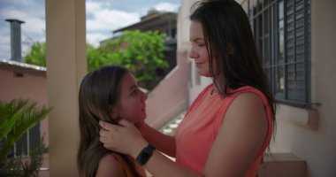 Arka planda yeşil ve pastel binalar olan Latin Amerika 'nın balkonunda kızını kucaklayan bir annenin yakın çekimi..