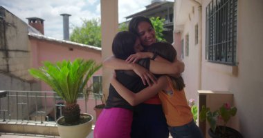 Anne, Güney Amerika 'da bir verandada sıcak, sevgi dolu bir kucaklaşmada iki kızını kucaklıyor ve hassas bir aile bağı anını yakalıyor.