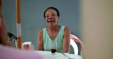 Yaşlı bir kadın açık hava yemeği sırasında ailesiyle bir anı paylaşırken sıcak bir şekilde gülümsüyor, çoklu nesiller arası bir toplantıda bağlantı ve mutluluk sergiliyor.