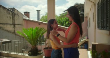 Anne, Güney Amerika 'da bir verandada gülümserken, küçük kızlarının yüzünü nazikçe tutuyor. Sevgisini ve aile bağını gösteriyor..