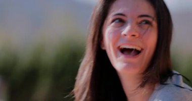 Latin Latin kadın gözleri kapalı ve başı hafifçe eğik gülümsüyor, kahkahaların ortasında, açık hava bulanık arka planıyla gülerken yakalandı.