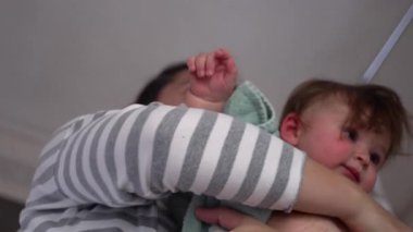 Anne banyodan sonra havluya sarılmış bebeği kucağında tutuyor, sıcak ev ortamında aile içi yakınlık, şefkat ve rahatlık anı yaşıyor.