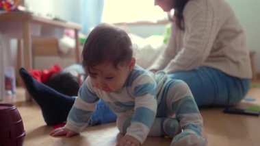 Bebek, aile yatak odasında renkli oyuncaklarla oynarken anne ve kardeşi yakınlarda merak ve erken öğrenme göstergesi olarak oynuyor.