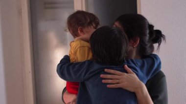 Anne, sıcak aile kucaklaşmasında iki çocuğu kucaklıyor. Bebek ve büyük kardeş, sevgi, şefkat ve evde güçlü duygusal bağlar gösteriyorlar.