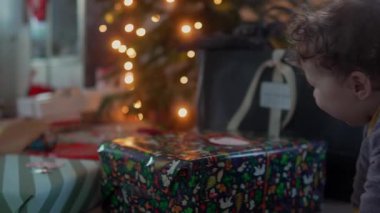 Ağacın yakınındaki büyük bir Noel hediyesine yaslanan bebek, Noel neşesi, sıcaklık ve mevsimsel kutlama beklentisiyle dolu şenlikli aile evi.