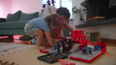 Evde oyuncak garajıyla oynayan iki kardeş, küçük çocuğun büyük kardeşinin oyun alanını istila etmesi, aile paylaşımının dinamikleri, kaynaşma ve hafif kardeş rekabeti.