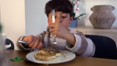 Çocuk ev mutfağının iç kısmında kahvaltı masasında çatal ve bıçakla waffle yaparken konsantre oluyor.