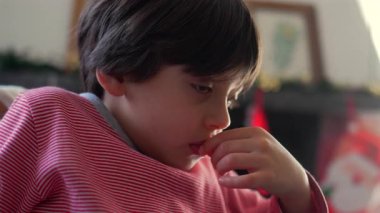 Kanepede oturan genç bir çocuk, düşünceli bir ifadeyle ve eli ağzının kenarında, odaklanma, konsantrasyon ve duyguyu her gün aile ortamında gösteriyor.