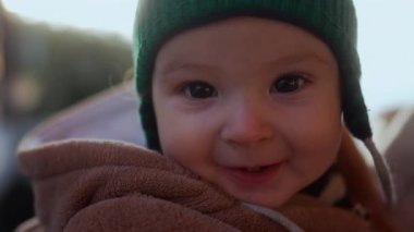 Bebek, parlak gözleriyle kameraya bakıyor. Ayı postu ceketi ve yeşil bere takıyor. Kışın çocuk, sıcakkanlı ve masum bir şekilde gülümsüyor.