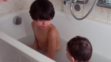 Ağabey küvette küçük kardeşe bakıyor. Evde sıcak bir aile banyosu sırasında.